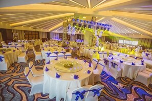 Een feestzaal met ronde tafels, stoelen en een podium met verlichting.