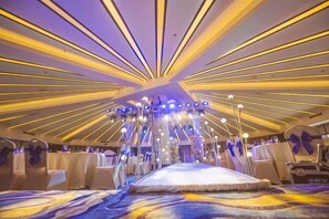 Una sala con un escenario central, mesas múltiples e iluminación radial en el techo.