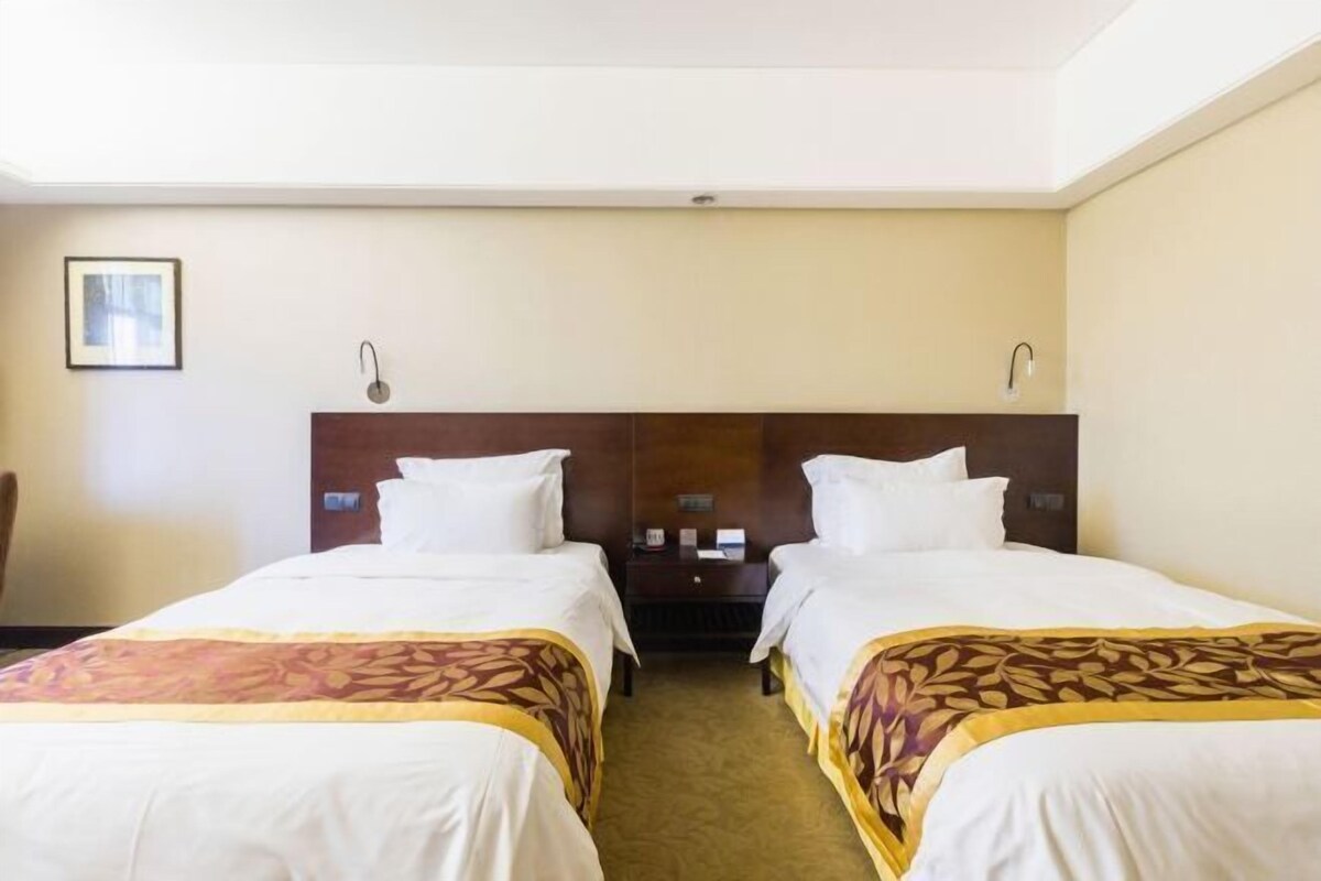 Een hotelkamer met twee bedden, een nachtkastje, een ingelijst beeld aan de muur en een lamp boven het nachtkastje.