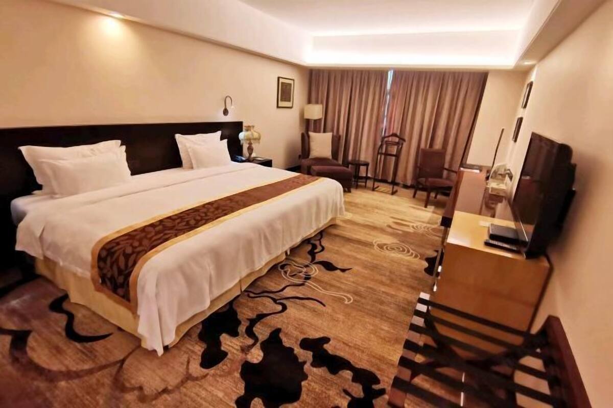 A hotel room with a large bed, a desk, a chair, a TV, and a lamp.
