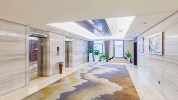 A modern hotel lobby with a marble floor, a reception desk, and a staircase leading to the upper floor.