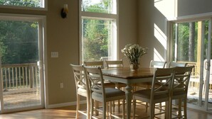 Un comedor con mesa y sillas de madera, ventanas amplias y vistas a zonas verdes.