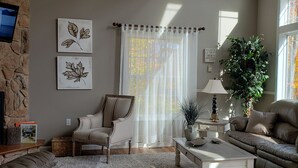 Una sala de estar acogedora con chimenea de piedra, un ventanal con cortinas translúcidas, un sofá cómodo y una mesa de centro.