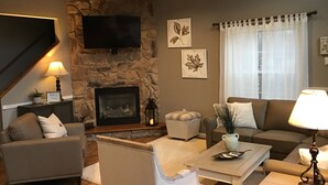 Una sala de estar acogedora con chimenea de piedra, televisor de pantalla plana y un espacio de descanso cómodo con sofá y sillones.