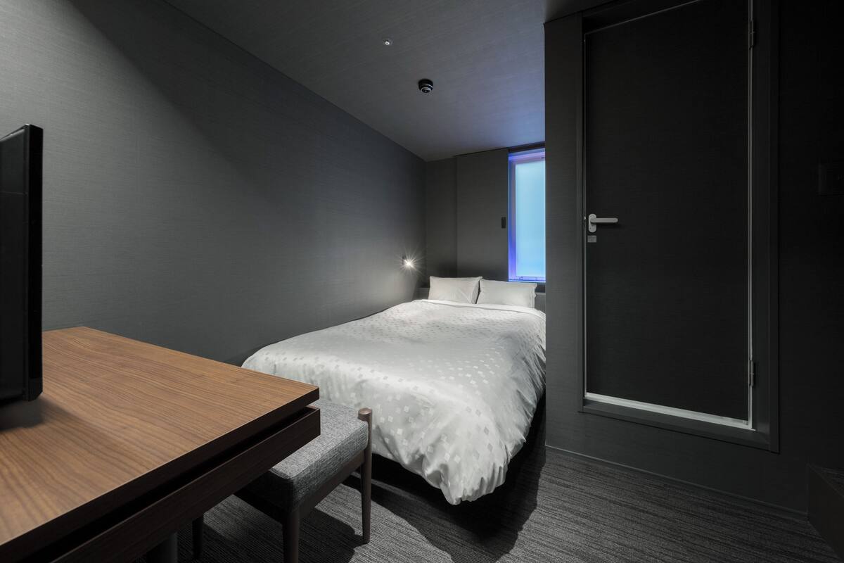 A modern hotel room with a bed, a desk, and a window.