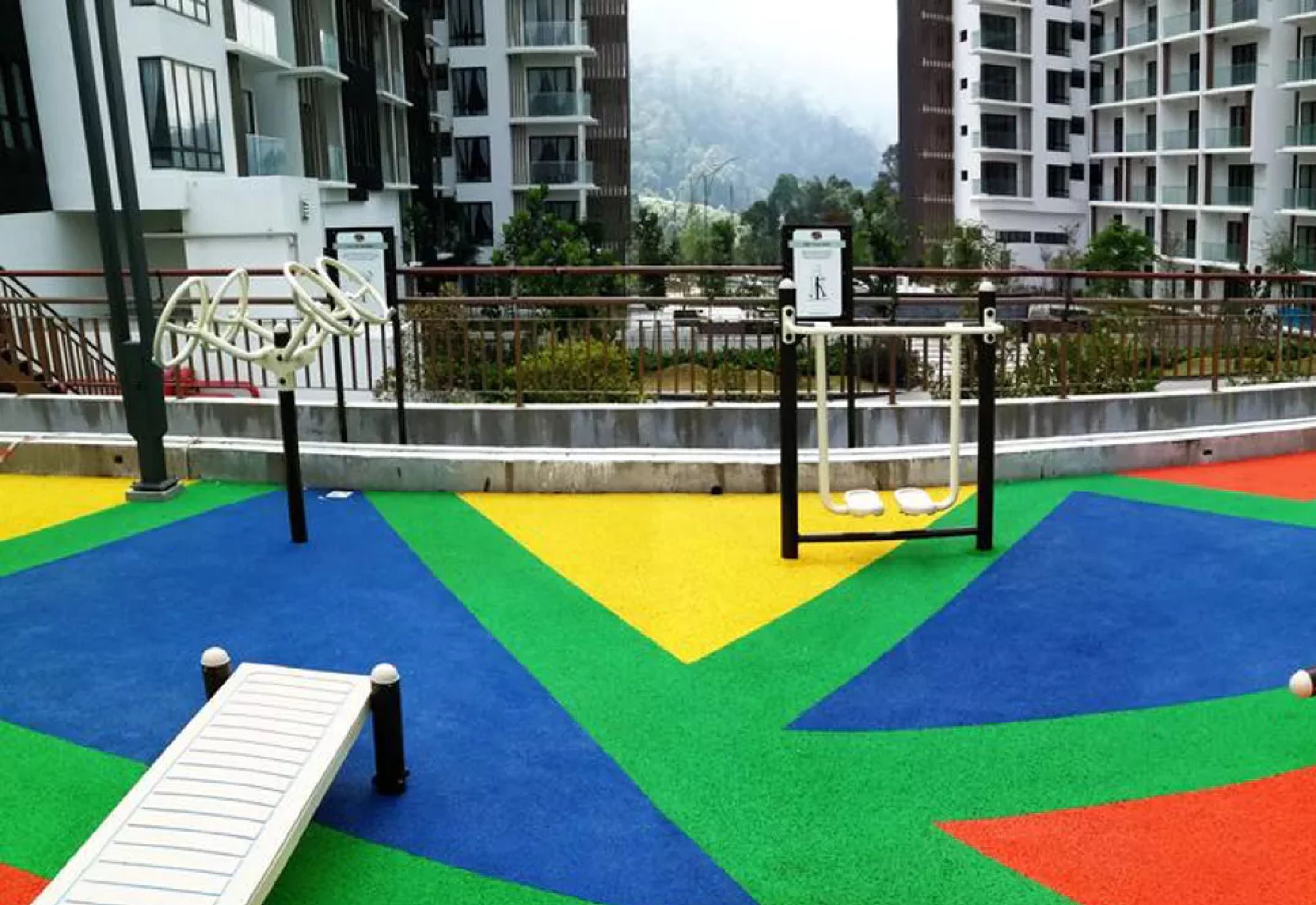 A playground with colorful mats and exercise equipment, surrounded by residential buildings.