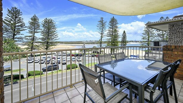 Un balcon avec une table et des chaises, donnant sur un parking et une plage.