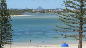 Une plage à l’eau claire, avec quelques personnes et une montagne en arrière-plan.