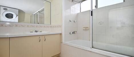 A bathroom with a built-in washing machine, a bathtub, and a shower enclosure.