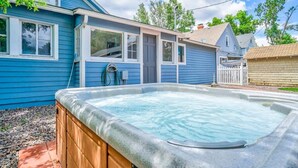 Un patio trasero con un jacuzzi, una terraza de madera y una casa con revestimiento azul y detalles blancos.