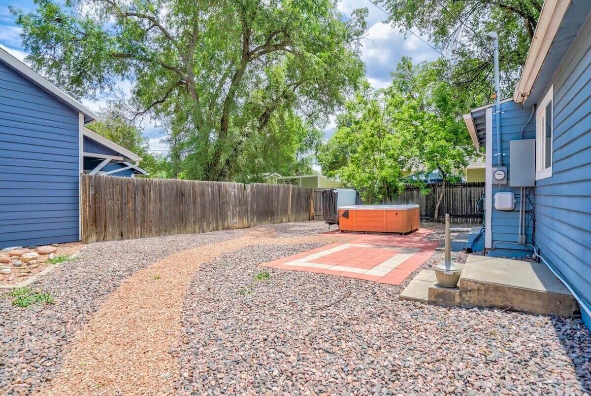 A backyard with a wooden fence, a hot tub, and a gravel path.