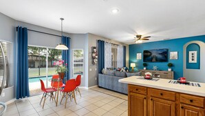 A modern kitchen with a central island, a dining area with red chairs, and a view of a swimming pool. - 2 Miles to Disney • Walk to Clubhouse • SOUTH-FACING Pool • Free Water Park (Kissimmee)