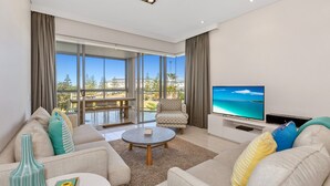 Een moderne woonkamer met een grote televisie, comfortabele zitplaatsen en uitzicht op de omgeving.