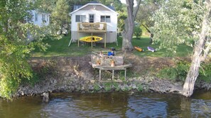 Una casa con terraza que da a un cuerpo de agua, rodeada de árboles y un muro de piedra.