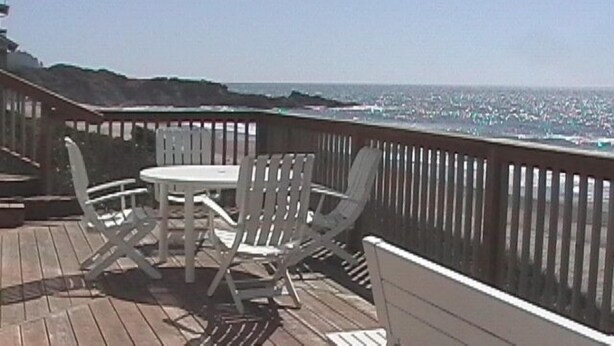 A wooden deck with a table and chairs, overlooking a beach and ocean. - Shearwater Beach Front Vacation Rental 3000 sqft (Depoe Bay)
