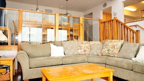 A living room with a sectional sofa, a wooden coffee table, and a staircase with wooden railings. - Shearwater Beach Front Vacation Rental 3000 sqft (Depoe Bay)