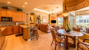 A spacious kitchen with wooden cabinets, a central island, and a dining area with a round table and chairs. - Beautifully Furnished Tommy Bahama Inspired Home (Marco Island)