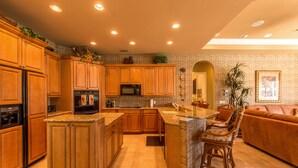 A spacious kitchen with wooden cabinets, a central island, and a dining area with chairs. - Beautifully Furnished Tommy Bahama Inspired Home (Marco Island)