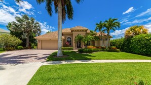 A two-story house with a tiled roof, a front lawn, and palm trees. - Beautifully Furnished Tommy Bahama Inspired Home (Marco Island)