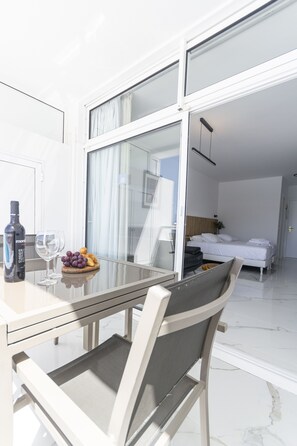 A modern hotel room with a glass door leading to a balcony. The room features a bed, a bedside table, and a chair. - Puerto Rico Gran Canaria: Beach and enjoyment at your fingertips (Mogán)