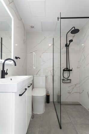 A modern bathroom with a white sink, toilet, and shower area. - Puerto Rico Gran Canaria: Beach and enjoyment at your fingertips (Mogán)