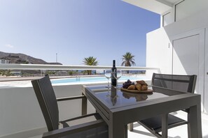 A balcony with a table set for two, overlooking a pool and a mountainous landscape. - Puerto Rico Gran Canaria: Beach and enjoyment at your fingertips (Mogán)