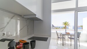 A modern kitchen with a large window overlooking a balcony with a table and chairs. - Puerto Rico Gran Canaria: Beach and enjoyment at your fingertips (Mogán)