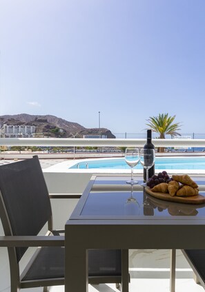 A table with a bottle of wine, two glasses, and a plate of croissants, overlooking a pool and a mountainous landscape. - Puerto Rico Gran Canaria: Beach and enjoyment at your fingertips (Mogán)