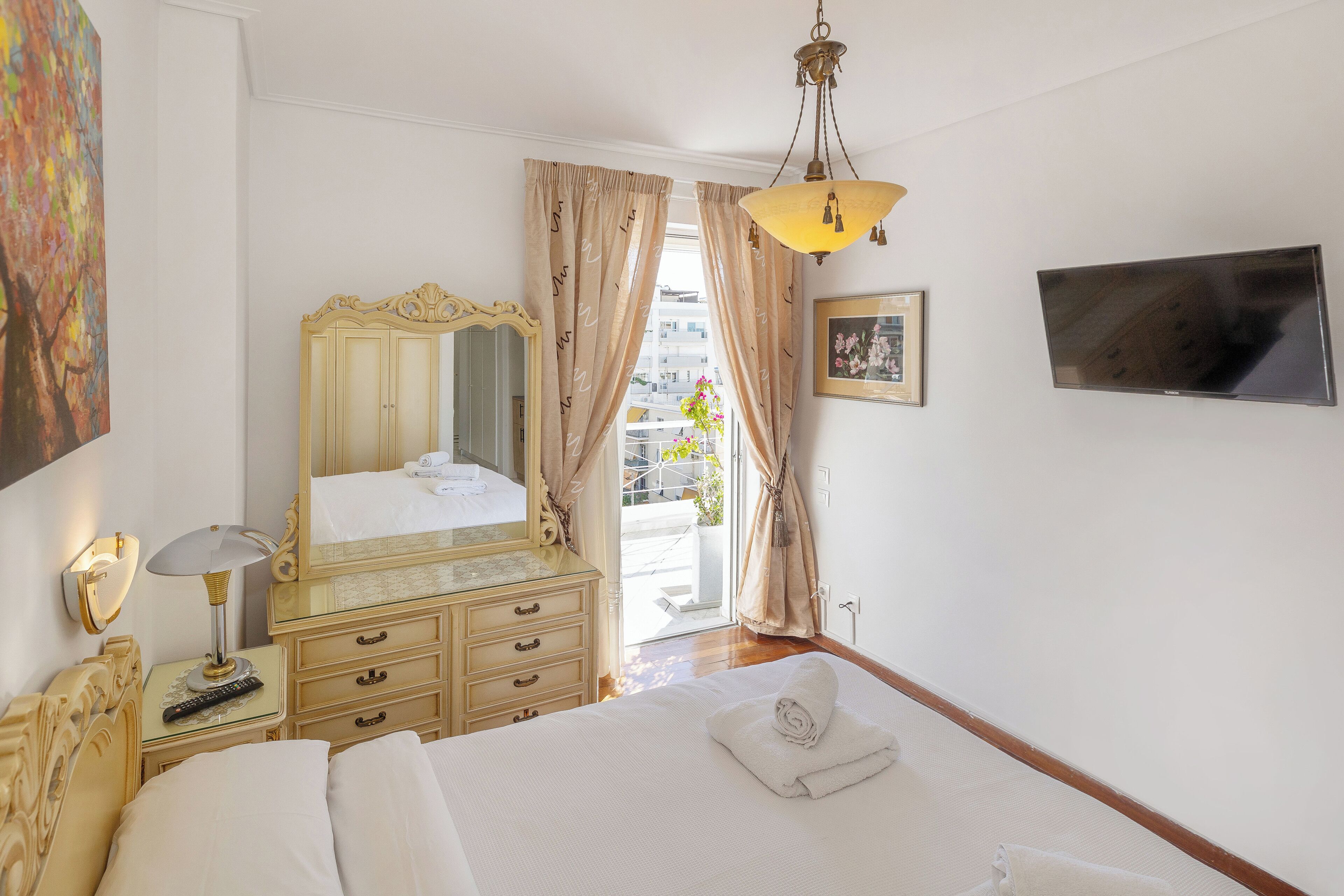 Une chambre d’hôtel avec un lit, une commode, un miroir, une lampe, une télévision et une fenêtre avec des rideaux.
