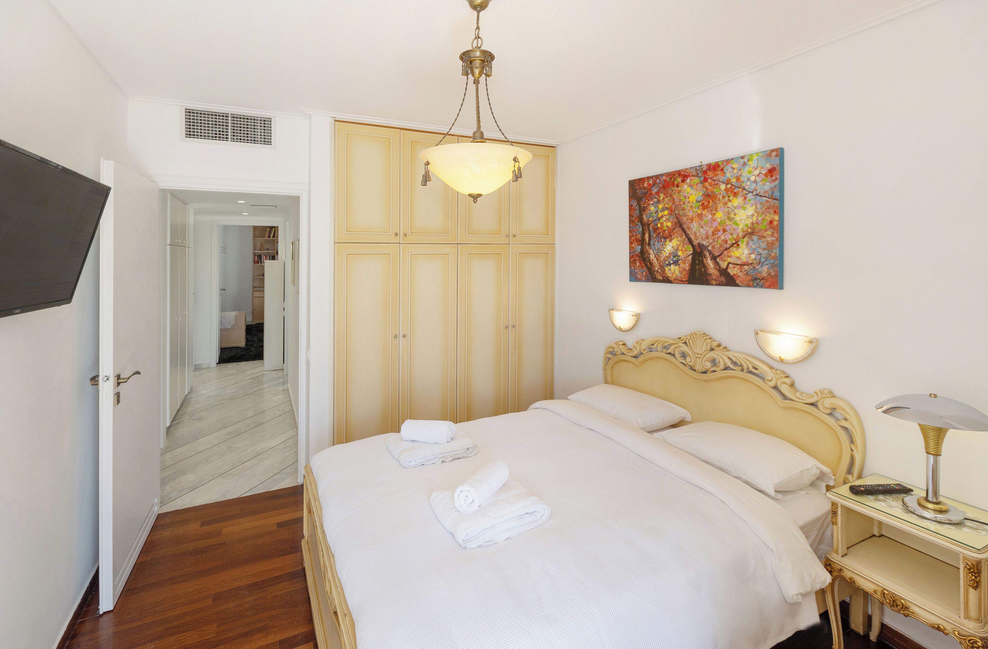 A bedroom with a bed, a bedside table with a lamp, a painting on the wall, and a wardrobe.