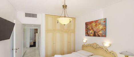 A bedroom with a bed, a bedside table with a lamp, a painting on the wall, and a wardrobe.