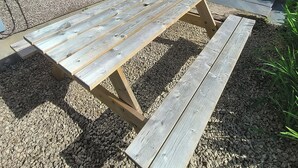 Ett picknickbord av trä med bänkar, ett fönster, en dörr och en stenmur.