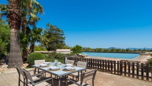 Un área de comedor al aire libre con una mesa preparada para cuatro personas, con vistas a una masa de agua y un paisaje montañoso.