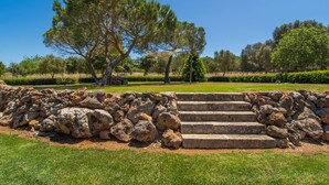 Una escalera de piedra que asciende hacia un muro de piedra, rodeada de césped y árboles en un entorno similar a un parque.