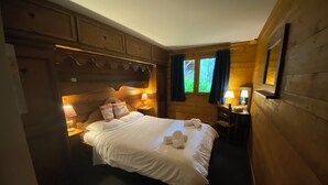 A cozy wooden cabin bedroom with a large bed, two bedside lamps, a small desk, and a window with curtains. - Arc 2000 Chalet, Peaceful Chalet By Slopes with Pool/Spa  (Bourg-Saint-Maurice)
