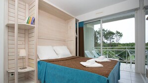 A bedroom with a bed, a nightstand, a bookshelf, and a balcony with chairs.