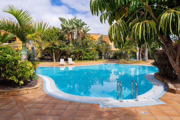 A swimming pool surrounded by palm trees and a tiled deck. - 3 bedroom villa in family complex with pools (Corralejo)