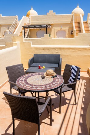 A round table with wicker chairs, a hat, sunglasses, and a drink on a terrace with a tiled floor and a yellow wall. - 3 bedroom villa in family complex with pools (Corralejo)