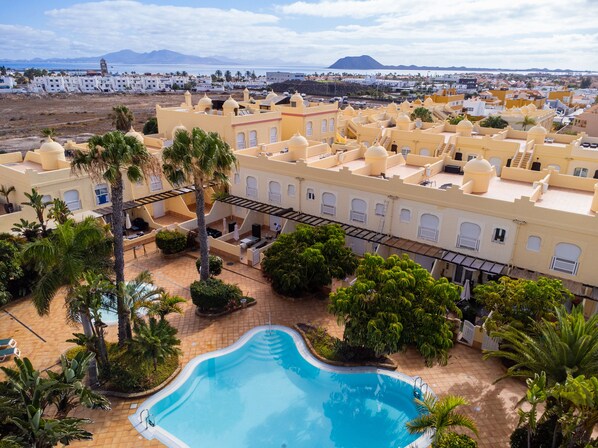 A resort with a swimming pool, palm trees, and a view of the sea and mountains.
