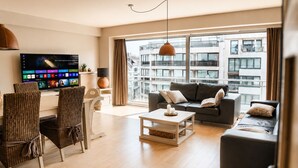Ein modernes Wohnzimmer mit großem Fernseher, Korbsesseln, einer Couch und einem Esstisch.