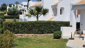 Un bâtiment moderne de couleur blanche, doté d’un jardin bien entretenu, comprenant un palmier et des haies soigneusement taillées.