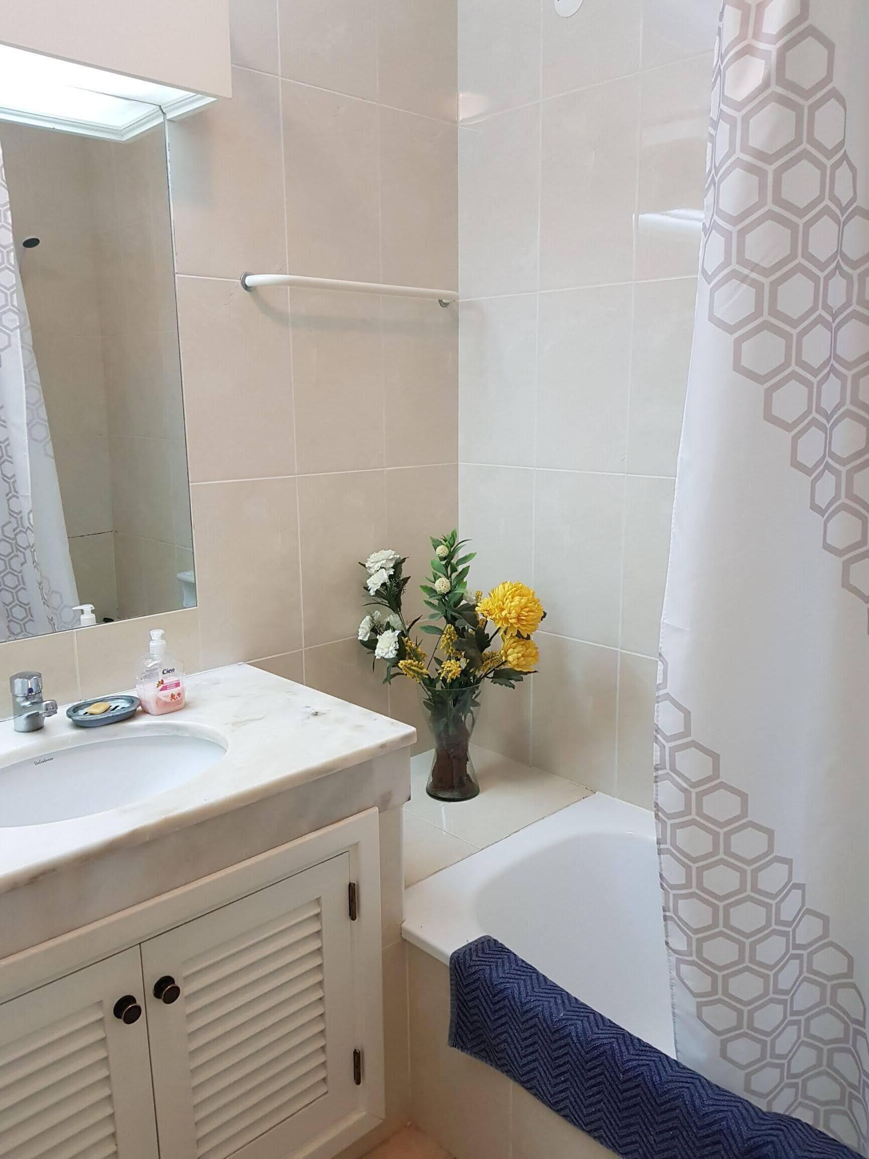 Een badkamer met een witte wastafel, spiegel en een douchegordijn met een geometrisch patroon.