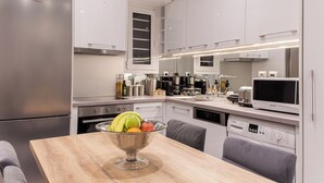 Une cuisine moderne avec des meubles blancs, des appareils en acier inoxydable et un coin repas comprenant une table et des chaises en bois.
