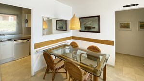 Cozinha moderna com lava-louças, sala de jantar com mesa de vidro e cadeiras de vime, e espelho fixado na parede.