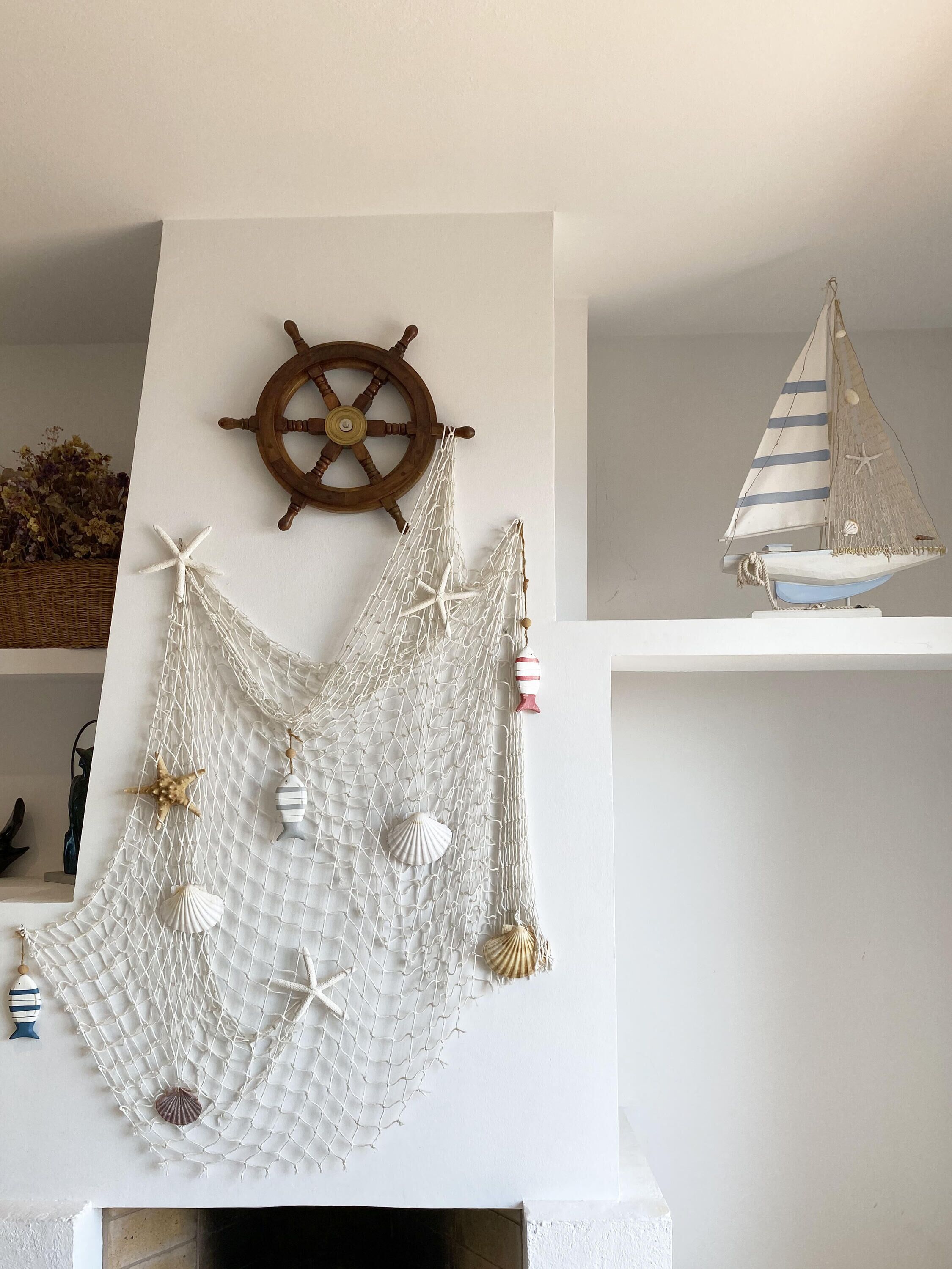 Un élément de décoration murale sur le thème de la navigation, comprenant un gouvernail de navire, un voilier et divers coquillages.