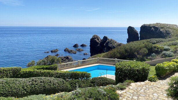 Uma piscina rodeada por vegetação exuberante e penhascos rochosos com vista para o mar.