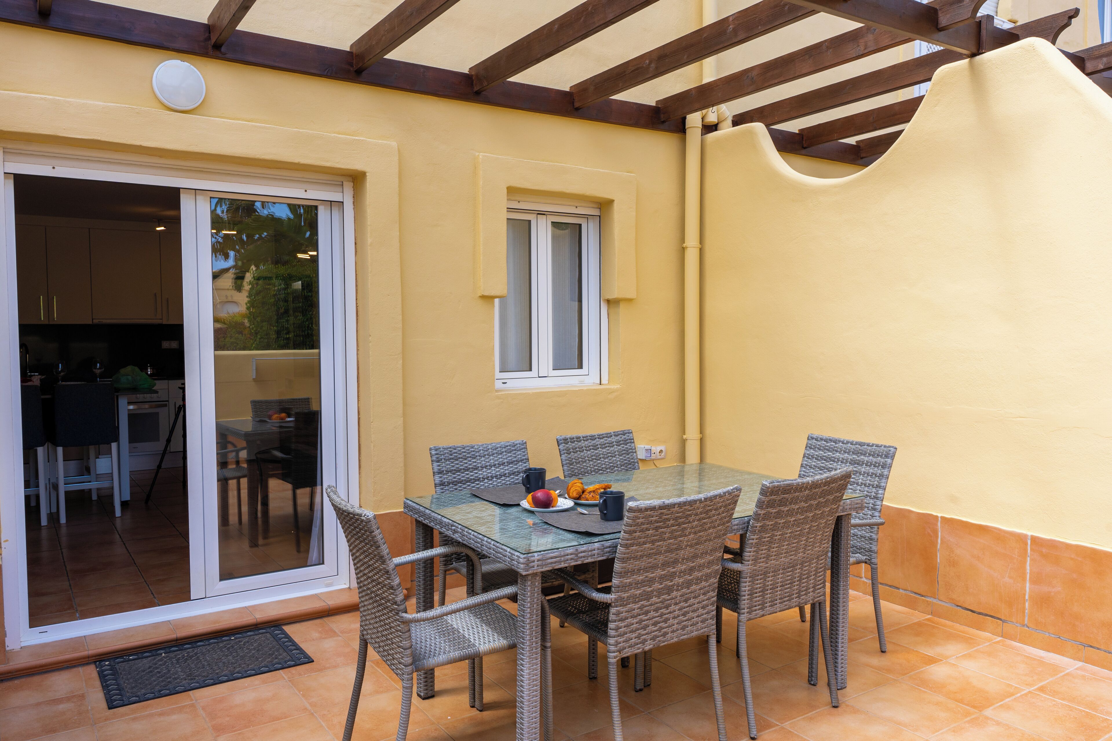 Une terrasse extérieure avec une table en verre et des chaises en osier, une porte-fenêtre coulissante et une petite fenêtre.