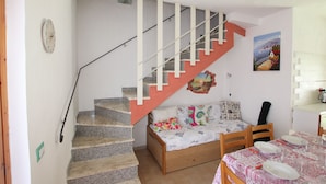 A bedroom with a bed, a wooden chair, a dining table set for two, and a staircase with a red handrail. - San Teodoro: 600 m. from the beach and the center, air conditioning, Wi-Fi  (San Teodoro)