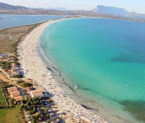 Vue aérienne d’une zone côtière avec une plage, des bateaux et des bâtiments le long du rivage.