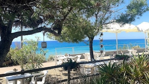 Ein Sitzbereich im Freien mit weißen Plastikstühlen und -tischen, mit Blick auf das klare, blaue Meer.